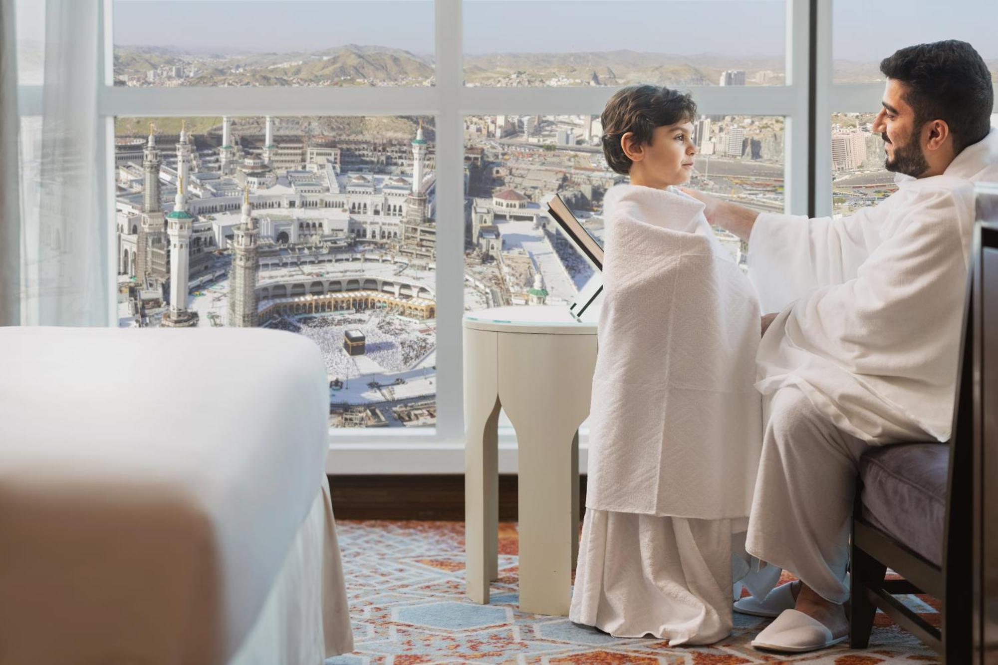 Swissotel Makkah La Meca Exterior foto The photo depicts a father and son sitting together in a hotel room. The father is wrapping a cloth around the boy, who appears to be preparing for a religious pilgrimage or ceremony, likely in the context of Hajj or Umrah. The background showcases a