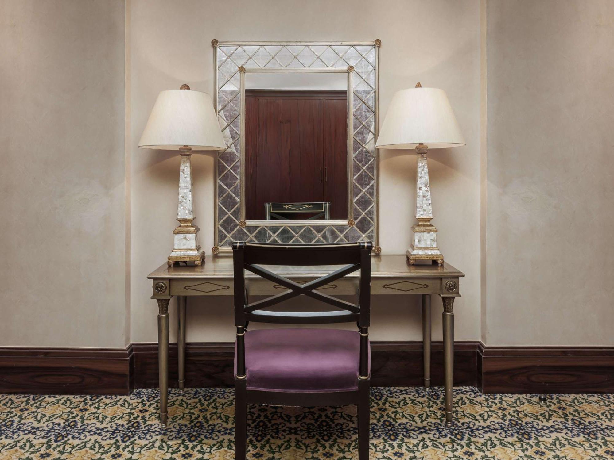 Swissotel Makkah La Meca Exterior foto The photo shows a small, elegantly decorated space featuring a vanity table with a mirror above it. The table is paired with a dark wooden chair that has a purple cushion. On either side of the mirror, there are tall, decorative lamps that provide so