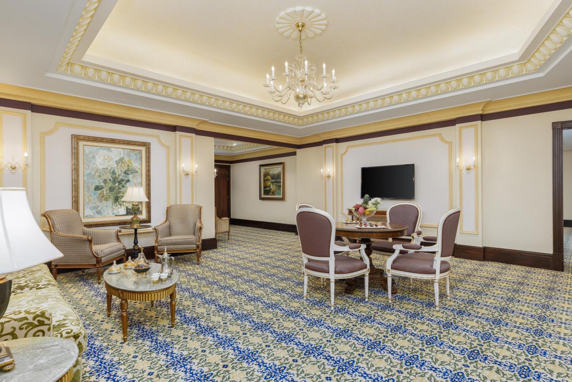 Swissotel Makkah La Meca Exterior foto The photo shows a luxurious interior space, likely a hotel suite or a high-end lounge area. It features a beautifully patterned carpet with blue and cream tones. The room is furnished with two elegant armchairs and a round dining table surrounded by 