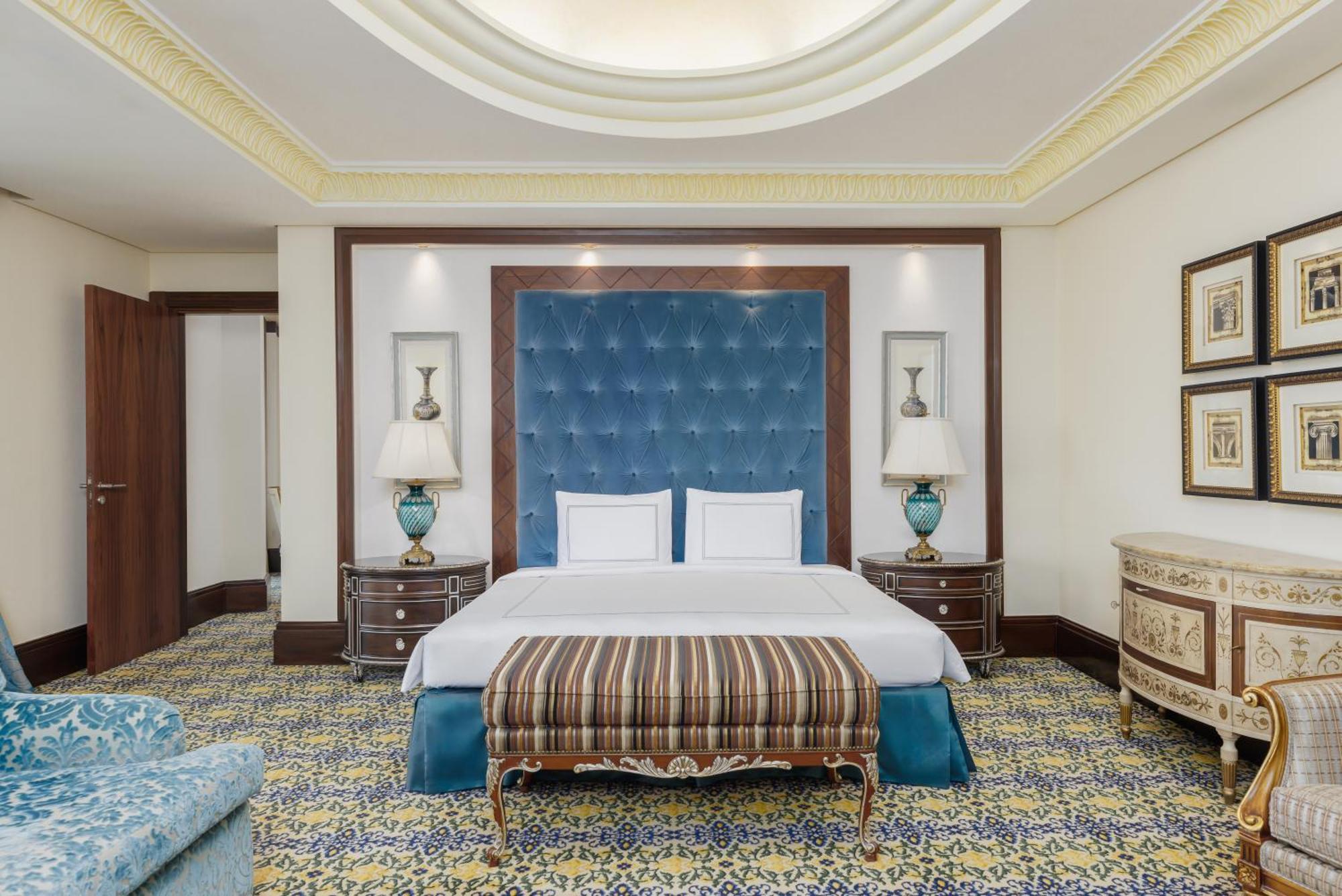 Swissotel Makkah La Meca Exterior foto The photo shows an elegantly designed hotel room. Central to the room is a large, comfortable bed with a blue tufted headboard. On either side of the bed are stylish bedside tables with lamps, featuring decorative turquoise bases. A decorative stripe