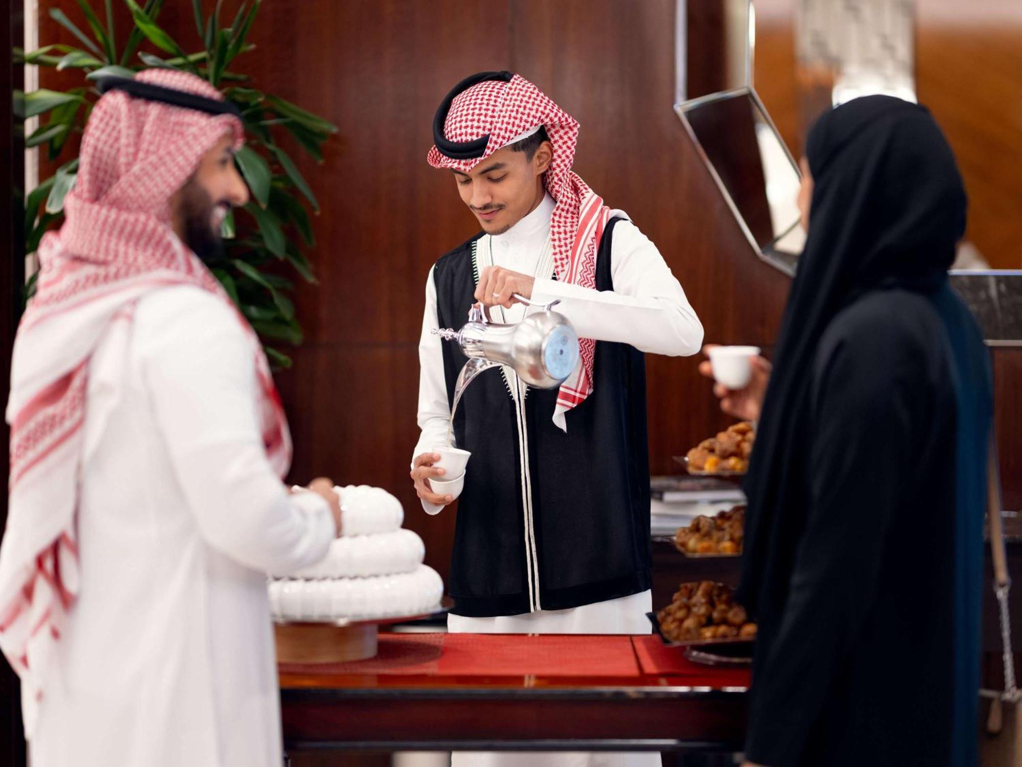 Swissotel Makkah La Meca Exterior foto The photo shows a traditional setting where two men and a woman are engaged in a cultural activity. One man, dressed in traditional attire with a red and white checkered headscarf (ghutrah), is pouring tea or coffee from a silver pot into small cups.