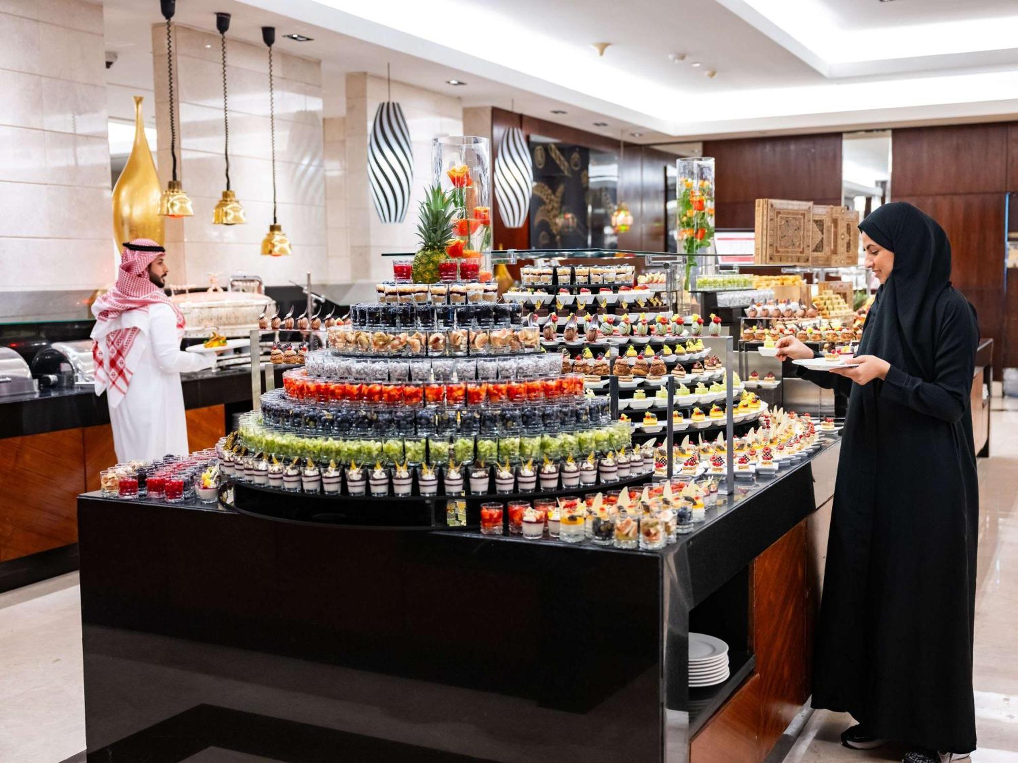 Swissotel Makkah La Meca Exterior foto The photo shows a luxurious buffet setup in a dining area. There is a prominent display of desserts arranged in a visually appealing manner, featuring various small containers filled with colorful treats, including fruit, creams, and pastries. A woma